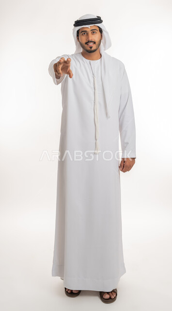 إحتواء وإمساك عنصر ما، مفهوم الاناقة و الاهتمام بالمظهر الخارجي, بورتريه لرجل عربي خليجي اماراتي يرتدي الكندورة و العمامة يعرض عنصر هولوجرامي ثلاثي الأبعاد، صورة الجسم بالطول الكامل, خلفية بيضاء