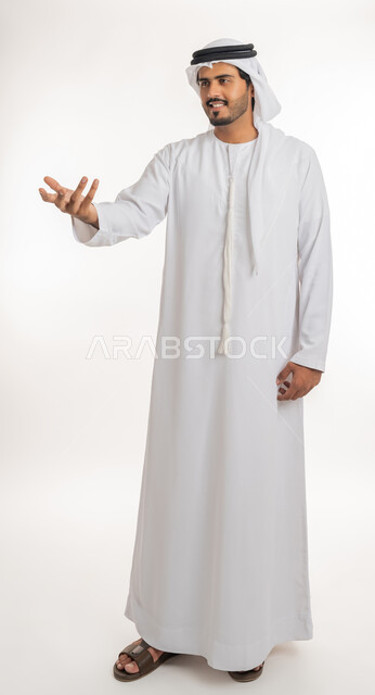 الإشارة إلى عنصر ما، بورتريه لرجل عربي خليجي اماراتي يرتدي الكندورة و الغترة البيضاء يمد يده للأمام يحاول التقاط عناصر هولوجرامية ثلاثية الأبعاد، محاولة الإحاطة والإمساك بشيء ما، الجسم بالطول الكامل، خلفية بيضاء