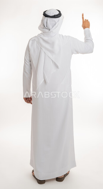 تحديد موقع معين، بورتريه من الخلف لرجل عربي خليجي اماراتي يرتدي الكندورة والغترة البيضاء يرفع يده للاعلى يشير بأصبع السبابة الى هدف محدد، الجسم بالطول الكامل، خلفية بيضاء