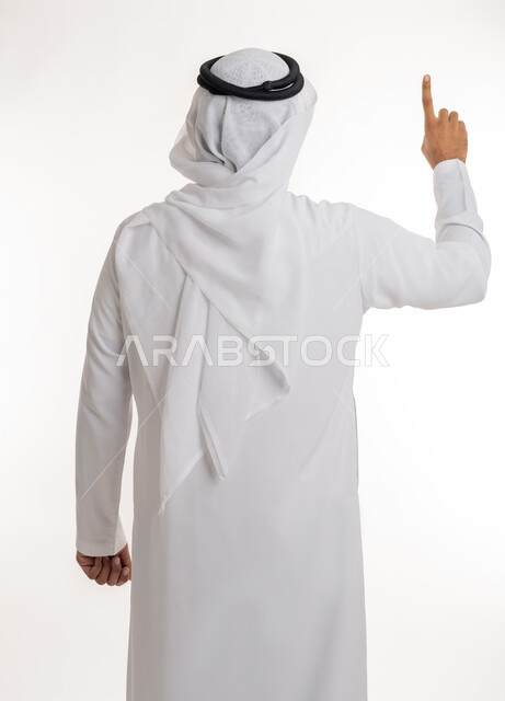 الإشارة إلى عنصر ما، بورتريه مقرب من الخلف لرجل عربي خليجي اماراتي يرتدي الكندورة والغترة البيضاء يرفع يده للاعلى يشير بأصبع السبابة الى هدف محدد، خلفية بيضاء