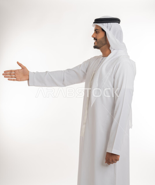 مفهوم الاستقبال والترحيب، إلقاء التحيه والسلام، بورتريه مقرب لرجل عربي خليجي إماراتي  يرتدي الكندورة والغترة البيضاء ينظر يمد يده بإيماءات المصافحة، التعارف و الصداقه وتكوين العلاقات، خلفية بيضاء