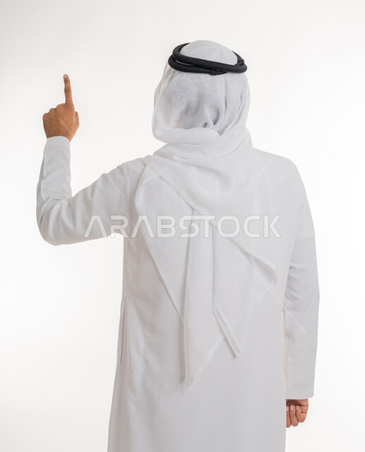 الإشارة إلى عنصر ما، بورتريه مقرب من الخلف لرجل عربي خليجي اماراتي يرتدي الكندورة والغترة البيضاء يرفع يده للاعلى يشير بأصبع السبابة الى هدف محدد، خلفية بيضاء