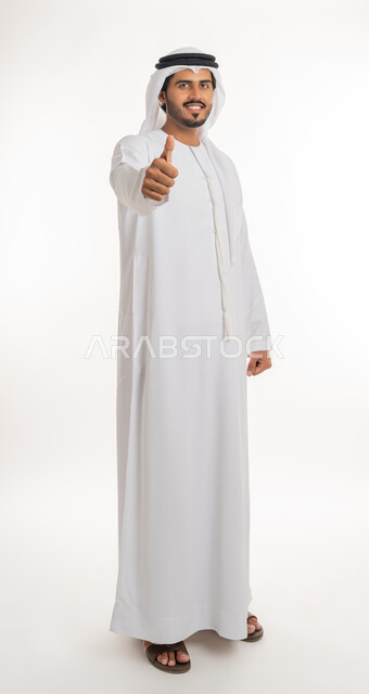 الرضا بالنتيجه الإمتياز والتميز، إيماءات وجه ويدين تدل على الموافقه والقبول، بورتريه مقرب لرجل عربي خليجي اماراتي يرتدي الثوب التقليدي الإماراتي والغترة البيضاء، يرفع أصبع الإبهام الى أعلى، الإعجاب والرضى والنجاح, الجسم بالطول الكامل، خلفية بيضاء