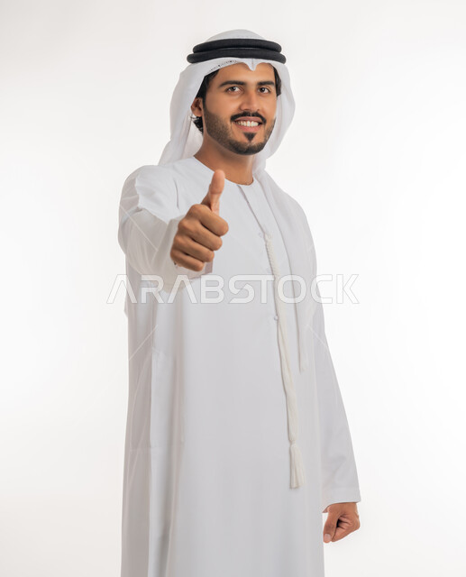 إيماءات وجه ويدين تدل على الموافقه والقبول، بورتريه مقرب لرجل عربي خليجي اماراتي يرتدي الثوب التقليدي الإماراتي والغترة البيضاء، يرفع أصبع الإبهام الى أعلى، الرضا بالنتيجه الإمتياز والتميز، الإعجاب والرضى والنجاح, خلفية بيضاء