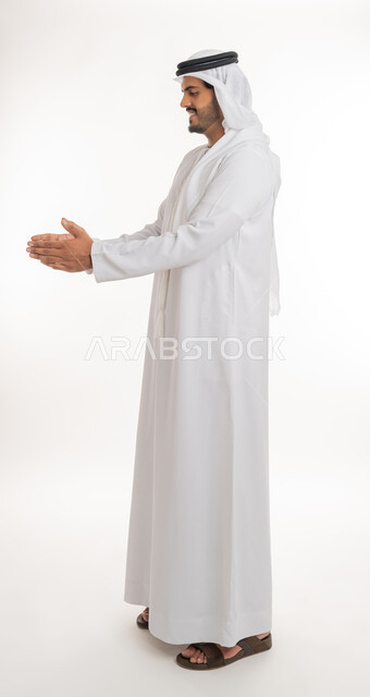 إحتواء وإمساك عنصر ما، مفهوم الاناقة و الاهتمام بالمظهر الخارجي, بورتريه لشاب عربي خليجي اماراتي يرتدي الكندورة و الغترة يفتح يديه لعرض عناصر هولوجرامية ثلاثية الأبعاد، صورة الجسم بالطول الكامل, خلفية بيضاء
