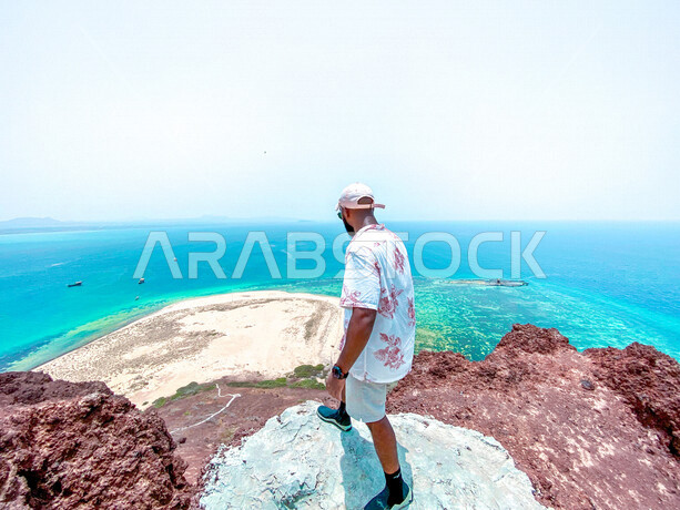 سائح عربي خليجي سعودي في رحلة إلى جزيرة جبل كُدُمبل واقعة في البحر الأحمر تتبع مركز القحمة في منطقة عسير بالمملكة العربية السعودية، الواجهة البحرية الطبيعية الخلابة بعسير في وضع النهار، السياحة بالسعودية