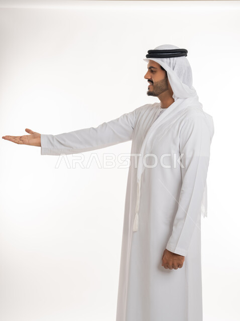 مفهوم الاناقة و الاهتمام بالمظهر الخارجي, محاولة رفع عنصر ما،  بورتريه مقرب من الجانب لرجل عربي خليجي امارتي يرتدي الكندورة و الغترة ينظر  يرفع كفه للاعلى يحمل عناصر هولوجرامية ثلاثية الأبعاد، خلفية بيضاء
