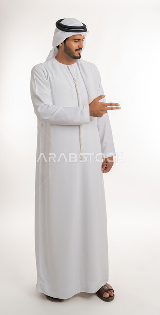 حركة اصبع وإشارات، الإشارة نحو اليمين، بورتريه لرجل عربي خليجي إماراتي يرتدي الكندورة والغترة الإماراتية يشير باصابعه نحو شيء ما، تحديد هدف معين، صورة الجسم بالطول الكامل, خلفية بيضاء