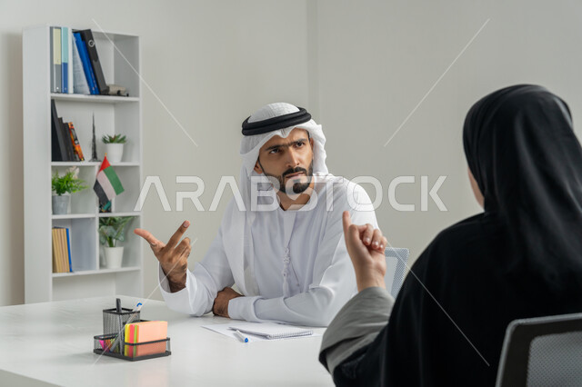 مفهوم التحاور وتبادل الأراء في خطط إنجاز الأعمال، إجراء مقابلة التعيين والتوظيف، صورة مقربة لمدير عربي خلجي إماراتي يرتدي الغترة والكندورة داخل المكتب يقوم بإجراء مقابلة عمل مع موظفة، مهن ووظائف إدارية مكتبية في الإمارات، المساواة بين المرأة والرجل