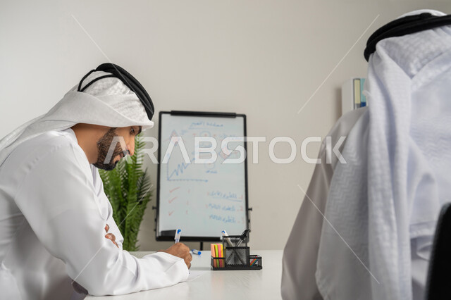 كتابة وتدوين الملاحظات، تبادل الأراء والافكار بين الموظفين، رجلان عربيان خليجيان إماراتيان يرتديان الغترة والكندورة يعقدان اجتماع داخل مقر الشركة، تعلم اساليب العمل والتطوير المهني، العمل الجماعي وروح الفريق الواحد، وضع الخطط الاستراتيجية لتحقيق الأهداف