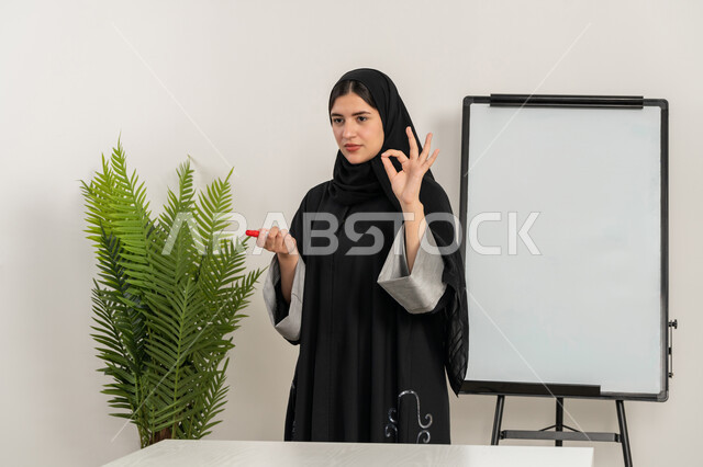 مدربة سعودية تستخدم السبورة لسهولة الشرح، ورشات عمل تدريبية مهنية، صورة مقربة لإمرأة عربية خليجية إماراتية ترتدي الحجاب والعباءة تقوم بتوضيح الخطوات لتحقيق الأهداف داخل مقر الشركة, تطوير استراتيجيات شركات الإمارات العربية المتحدة، تعلم اساليب العمل والتطوير المهني