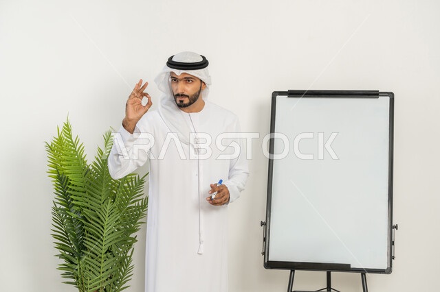 Learn business methods and professional development, use of whiteboard for easy explanation, professional training workshops, development of strategies of UAE companies, close-up of an Arab Gulf Emirati man wearing a ghutra and kandura explaining the steps to achieve goals inside the company headquarters