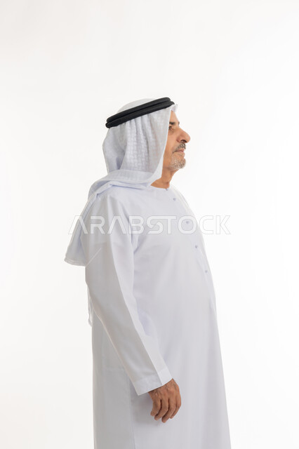 النظر الى شيء ما بإيماءات الجدية، التقدم بالعمر والهيبة والوقار، بورتريه من الجانب لرجل كبير بالسن عربي خليجي إماراتي يرتدي الكندورة, الاهتمام بالأناقة والمظهر الخارجي، الوقوف باستقامة وثبات، مفهوم الرجولة العربية, خلفية بيضاء