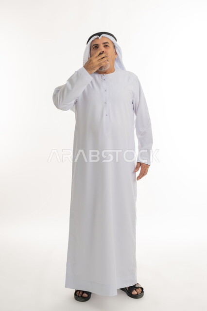 الإحساس بالإرهاق و الحاجه الى النوم والراحه ,بورتريه لرجل كبير السن عربي خليجي اماراتي يرتدي الكندورة والغترة يضع يده على فمه بإيماءات تدل على النعاس, التثاؤب والتعب والشعور بالكسل والخمول، الطول الكامل للجسم, خلفية بيضاء