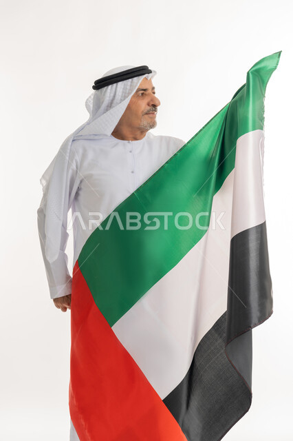 يوم استقلال الإمارات، بورتريه لرجل عربي خليجي إماراتي يرتدي الكندورة والغترة البيضاء يحمل علم الإمارات العربية المتحدة وينظر إليه، الاعتزاز والفخر بإنجازات البلاد، هوية اليوم الوطني الاماراتي 51، الإحتفال باليوم الوطني الإماراتي، خلفية بيضاء