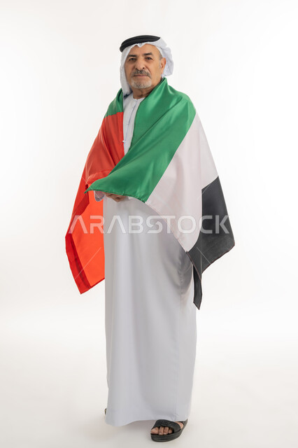 هوية اليوم الوطني الاماراتي 51، الإحتفال باليوم الوطني الإماراتي، بورتريه لرجل عربي خليجي إماراتي يرتدي الكندورة والغترة يحمل علم الإمارات العربية المتحدة على ظهره، ذكرى الإستقلال في 2 ديسمبر, الاعتزاز والفخر بإنجازات البلاد، الطول الكامل للجسم، خلفية بيضاء