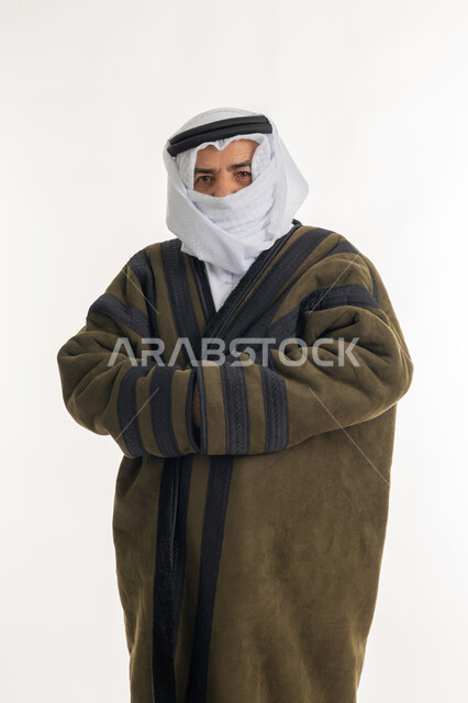 الشعور بالصقيع والقشعريرة والتجمد، إيماءات وجه ويدين تدل على البرد الشديد، بورتريه لرجل مسن عربي خليجي اماراتي  يرتدي الفروة والغترة التقليدية يقوم بتغطية انفه وتدفئة يديه، ارتداء الملابس الدافئة لكبار السن، الأجواء الشتوية الباردة، خلفية بيضاء