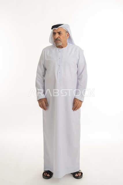 الشعور بالعصبية والضجر، تعابير العبوس والانزعاج، نظرات التحدي والغضب، بورتريه لرجل عربي خليجي إماراتي كبير بالسن يرتدي الغترة والكندورة الإماراتية، النظر الى شيء ما بايماءات السخط والتذمر، مفهوم عدم القبول والرضا، الطول الكامل للجسم، خلفية بيضاء