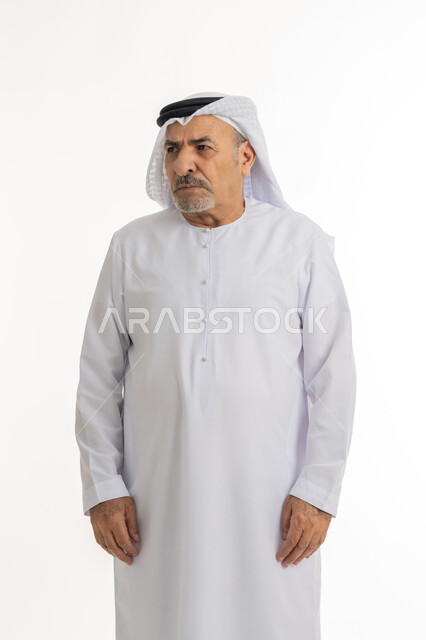 مفهوم عدم القبول والرضا، الشعور بالعصبية والضجر، تعابير العبوس والانزعاج، نظرات التحدي والغضب، بورتريه لرجل عربي خليجي إماراتي كبير بالسن يرتدي الغترة والكندورة الإماراتية، النظر الى شيء ما بايماءات السخط والتذمر، خلفية بيضاء