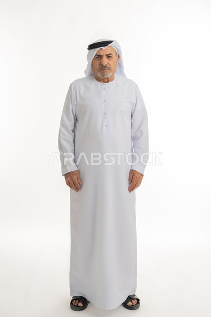 الشعور بالعصبية والضجر، تعابير العبوس والانزعاج، نظرات التحدي والغضب، بورتريه لرجل عربي خليجي إماراتي كبير بالسن يرتدي الغترة والكندورة الإماراتية، النظر الى الكاميرا بايماءات السخط والتذمر، مفهوم عدم القبول والرضا، الطول الكامل للجسم، خلفية بيضاء