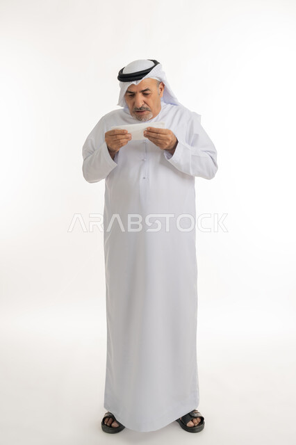 التعب والمرض والإصابة بالزكام و, بورتريه لرجل كبير السن عربي خليجي اماراتي يرتدي الغترة والكندورة يمسك المنديل بيديه ويغطي أنفه، ظهور أعراض الانفلونزا والعطاس بشكل متكرر، ضرورة الحصول على الراحة وأخذ العلاج المناسب, الجسم بالطول الكامل، خلفية بيضاء