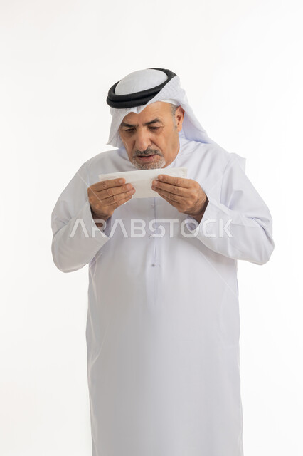 الشعور بالمرض و الزكام والحاجة الى العلاج والدواء, التهاب الأنف التحسسية وظهور أعراض الأنفلونزا, بورتريه لرجل كبير بالسن عربي اماراتي خليجي يرتدي الغترة والكندورة يضع يديه على وجهه بإيماءات العطاس, استخدام المناديل الورقيه للعطس, خلفية بيضاء