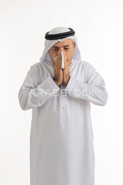 إيماءات الألم والتعب والمرض, بورتريه  لرجل كبير السن عربي خليجي اماراتي يرتدي الغترة والكندورة يمسك المنديل بيديه ويغطي أنفه، الحاجة للراحة وأخذ العلاج المناسب, الإصابة بالانفلونزا والعطاس والإحساس بأعراض الزكام، خلفية بيضاء