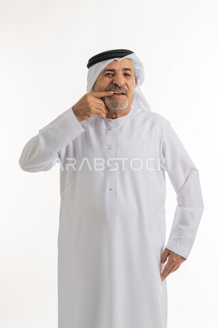 الحاجة لزيارة طبيب الأسنان, بورتريه لرجل كبير بالسن عربي خليجي اماراتي يرتدي الكندورة والغترة يضع يده على فمه, الاشارة إلى الفم بإيماءات الانزعاج والألم, مشاكل التهاب اللثة, طلب العلاج والمساعدة, خلفية بيضاء