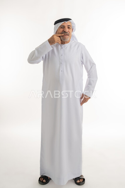 مشاكل التهاب اللثة, طلب العلاج والمساعدة, الحاجة لزيارة طبيب الأسنان, بورتريه لرجل كبير بالسن عربي خليجي اماراتي يرتدي الكندورة والغترة يضع يده على فمه, الاشارة إلى الفم بإيماءات الانزعاج والألم, صورة الجسم بالطول الكامل, خلفية بيضاء