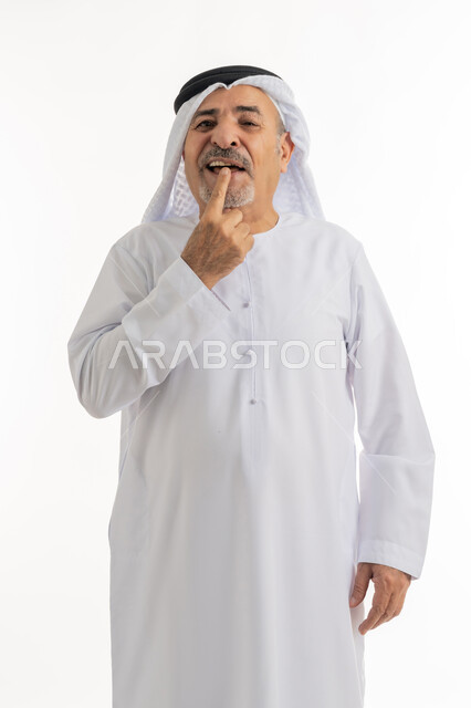طلب العلاج والمساعدة, الحاجة لزيارة طبيب الأسنان, بورتريه لرجل كبير بالسن عربي خليجي اماراتي يرتدي الكندورة والغترة يضع يده على فمه, الاشارة إلى الفم بإيماءات الانزعاج والألم, مشاكل التهاب اللثة, خلفية بيضاء