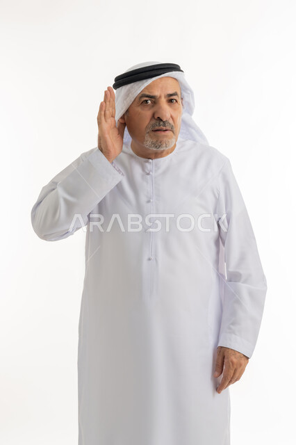 إيماءات التركيز والاستماع لفهم الكلام بشكل واضح، الحاجة لمراجعة طبيب الأذن لتركيب السماعات الطبية, بورتريه لرجل كبير السن عربي خليجي إماراتي يرتدي الغترة والكندورة يمسك أذنه بيده ويعاني من ضعف السمع، خلفية بيضاء