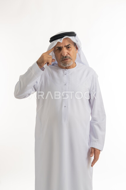 تعابير الجدية والحزم، الوقوف والنظر إلى الكاميرا بإيماءت العصبية والغضب، بورتريه لرجل عربي خليجي إماراتي كبير بالسن يرتدي الكندورة والغترة الإماراتية يشير بإصبعه إلى رأسه، رجاحة العقل والتفكير،  خلفية بيضاء