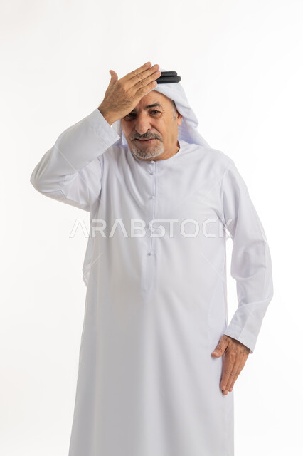 وضع اليد على الرأس بتعابير تذكر شيء ما بشكل مفاجئ، إيماءات خيبة الأمل والمعاناة مع النسيان، بورتريه مقرب لرجل عربي خليجي إماراتي كبير بالسن يرتدي الكندورة الإماراتية التقليدية والغترة يقف ويشعر بالانزعاج، خلفية بيضاء