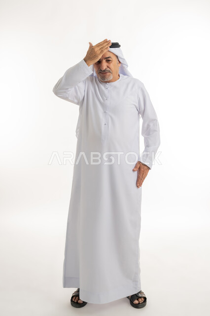 إيماءات خيبة الأمل والمعاناة مع النسيان، بورتريه مقرب لرجل عربي خليجي إماراتي كبير بالسن يرتدي الكندورة الإماراتية التقليدية والغترة يقف ويشعر بالانزعاج، وضع اليد على الرأس بتعابير تذكر شيء ما بشكل مفاجئ، الطول الكامل للجسم، خلفية بيضاء