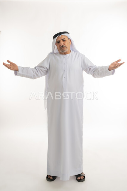 التساؤل والإستغراب والاستفسار عن أمر ما، الغموض وعدم الوضوح، الإستفهام حول موضوع معين, بورتريه لرجل عربي خليجي اماراتي يرتدي الكندورة والغترة يرفع يديه نحو الأعلى بإيماءات الحيرة عدم المعرفة, الطول الكامل للجسم، خلفية بيضاء