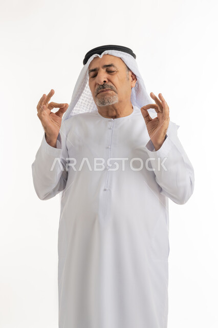 النظر للكاميرا بتعابير السعادة والرضا، بورتريه لرجل عربي خليجي إماراتي كبير بالسن يرتدي الكندورة الإماراتية والغترة يقف ويرفع يديه بإيماءات الموافقة، إشارات يدين تدل على علامة الجودة والإعجاب، خلفية بيضاء