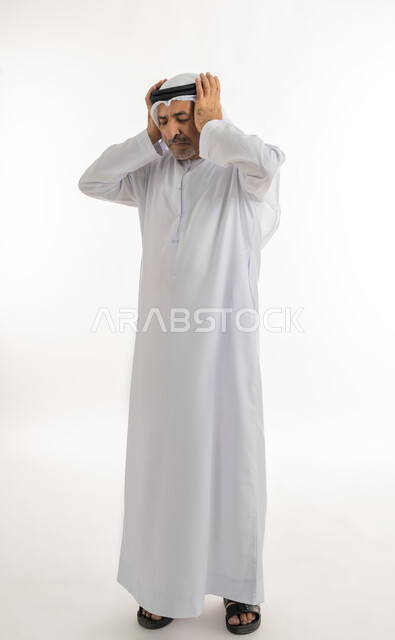 الحاجة إلى الهدوء والسكون، إيماءات الاضطراب والانزعاج من الصوت العالي, بورتريه لرجل كبير السن عربي خليجي إماراتي يرتدي الغترة والكندورة يغلق أذنيه بأصابعه للتخفيف من الضجيج المحيط به، الجسم بالطول الكامل، خلفية بيضاء