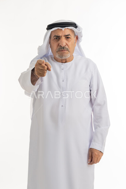 Gestures of anger and nervousness, asking to stop doing wrong, portrait of an elderly Arab Emirati Gulf man wearing a kandura and ghutra raising his index finger up to identify someone (you), feeling annoyed and wanting revenge, blaming and accusing, white background
