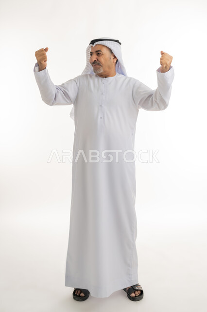 تحقيق الاهداف و إنجاز المهامات, الإعجاب والرضا و الشعور بالسعاده، بورتريه لرجل كبير بالسن عربي اماراتي خليجي يرتدي الكندورة الاماراتية والغترة ويرفع يديه فرحا بالنصر, ايماءات وجه ويدين تدل على الفوز و الكسب, علامة الفرح والقوه, صورة الجسم بالكامل، خلفية بيضاء