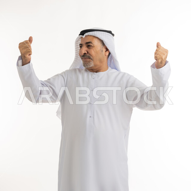 الإعجاب والرضا و الشعور بالسعاده، بورتريه لرجل كبير بالسن عربي اماراتي خليجي يرتدي الكندورة الاماراتية والغترة ويرفع يديه فرحا بالنصر, ايماءات وجه ويدين تدل على الفوز و الكسب, علامة الفرح والقوه, تحقيق الاهداف و إنجاز المهامات,،خلفية بيضاء