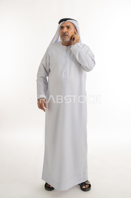 Trying to find a solution to problems, looking up carefully and planning for the future, portrait of an elderly Arab Gulf Emirati man wearing a ghutra and kandura, putting his hand on his face with an expression of thinking, Absent-mindedness and making decisions with concentration, full body length, white background