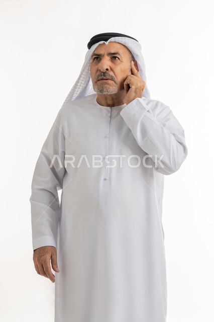 شرود الذهن واتخاذ القرارات بتركيز, محاولة إيجاد حل للمشكلات, النظر الى الاعلى بتمعن والتخطيط للمستقبل, بورتريه لرجل كبير السن عربي خليجي إماراتي يرتدي الغترة والكندورة يضع يده على وجهه بتعابير التفكير, خلفية بيضاء