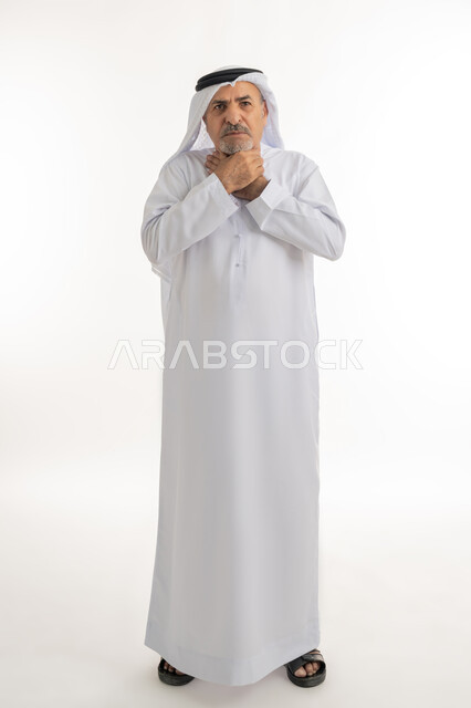 الاحساس بألم البلعوم, الحاجة إلى العلاج والدواء, مفهوم الاهتمام بالصحة, الاصابة بنزلة برد والتهاب الحلق، بورتريه لرجل كبير بالسن عربي خليجي إماراتي يرتدي الكندورة والغتره يضع يديه على حلقه ويشعر بالاختناق, الطول الكامل للجسم، خلفية بيضاء