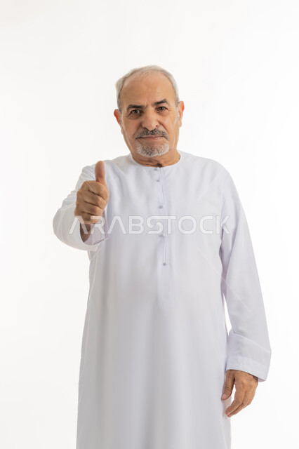 إيماءات الإعجاب والرضا، الاهتمام بالأناقة والمظهر الخارجي، بورتريه لرجل كبير بالسن عربي خليجي إماراتي يرتدي الكندورة ينظر الى الكاميرا يرفع إصبع السبابة للاعلى بتعابير القبول والفرح والسرور، خلفية بيضاء