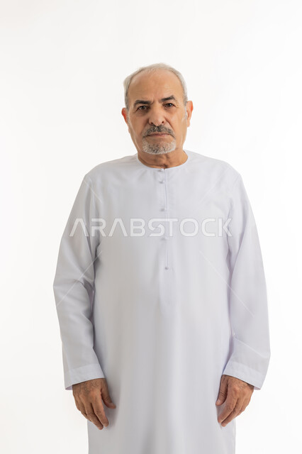 التقدم بالعمر والهيبة والوقار، النظر إلى الكاميرا يإيماءات الجدية والحزم، مفهوم الرجولة العربية, بورتريه لرجل كبير بالسن عربي خليجي اماراتي يرتدي الكندورة يقف باستقامة بتعابير الثقة بالنفس, الأناقه والاهتمام بالمظهر الخارجي، خلفية بيضاء