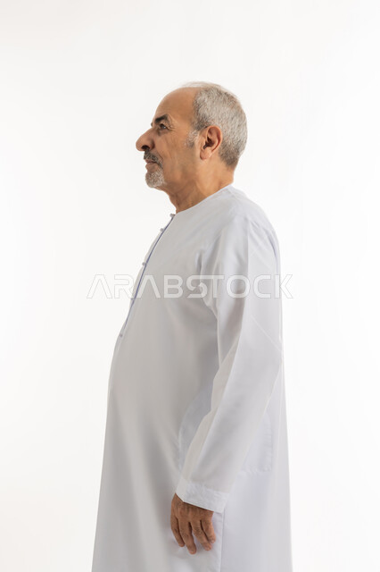 الاهتمام بالأناقة والمظهر الخارجي، الوقوف باستقامة وثبات، مفهوم الرجولة العربية, النظر الى شيء ما بإيماءات الجدية، التقدم بالعمر والهيبة والوقار، بورتريه من الجانب لرجل كبير بالسن عربي خليجي إماراتي يرتدي الكندورة, خلفية بيضاء