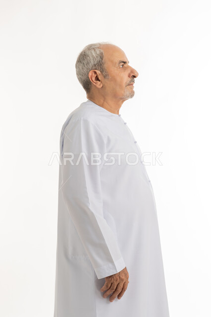 النظر الى شيء ما بإيماءات الجدية، التقدم بالعمر والهيبة والوقار، بورتريه من الجانب لرجل كبير بالسن عربي خليجي إماراتي يرتدي الكندورة, الاهتمام بالأناقة والمظهر الخارجي، الوقوف باستقامة وثبات، مفهوم الرجولة العربية, خلفية بيضاء