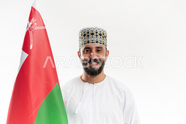 الفخر وإعتزاز بالهوية الوطنية، حب الوطن والانتماء إليه، إحياء ذكرى تأسيس الدولة 1775 م، العلم الوطني للبلاد، بورتريه  لرجل عربي خليجي عماني يرتدي الدشداشة و الكمة العمانية التقليدية يحتفل بذكرى اليوم الوطني العماني 18 نوفمبر، خلفية بيضاء