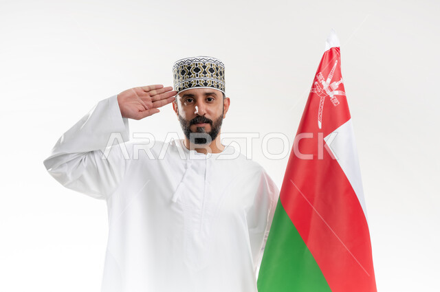 الفخر وإعتزاز بالهوية الوطنية، حب الوطن والانتماء إليه، إحياء ذكرى تأسيس الدولة 1775 م، العلم الوطني للبلاد، بورتريه  لرجل عربي خليجي عماني يرتدي الدشداشة و الكمة العمانية التقليدية يحتفل بذكرى اليوم الوطني العماني 18 نوفمبر، خلفية بيضاء