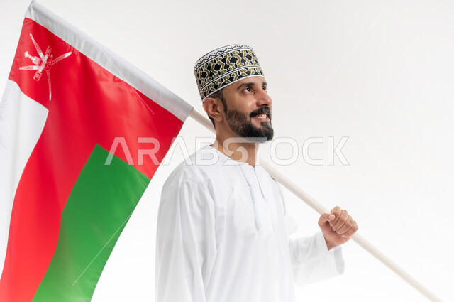 الفخر وإعتزاز بالهوية الوطنية، حب الوطن والانتماء إليه، إحياء ذكرى تأسيس الدولة 1775 م، العلم الوطني للبلاد، بورتريه  لرجل عربي خليجي عماني يرتدي الدشداشة و الكمة العمانية التقليدية يحتفل بذكرى اليوم الوطني العماني 18 نوفمبر، خلفية بيضاء
